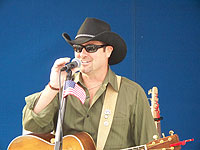 man with guitar and singing into microphone with small american flag attached
