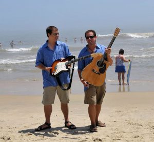 2 men with guitars on the beach