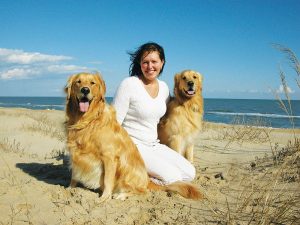 a woman sitting on a beach with three dogs