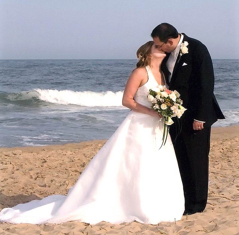 a bride and groom kissing on the beach