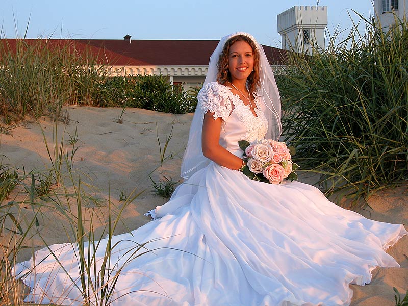 a woman in a wedding dress sitting in the sand